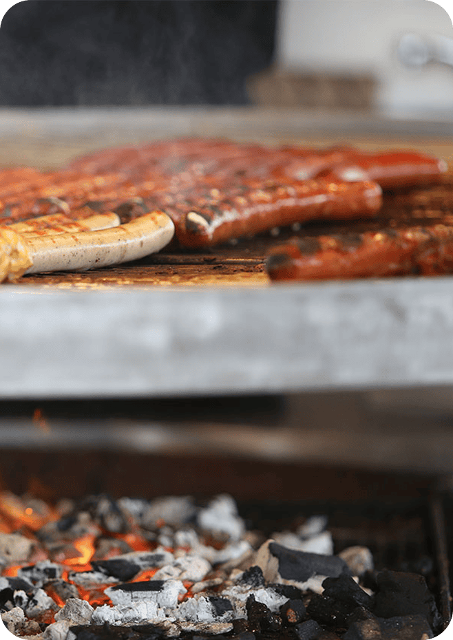 Gegrilde spareribs en worst op barbecue, rook en gloeiende houtskool, perfect voor barbecuefeest.